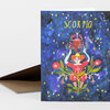 A folded greeting card with the word "SCORPIO" in yellow at the top and an illustrated scorpion held above a figure surrounded by flowers and stars.