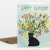 A greeting card with the text "HAPPY BIRTHDAY!" above an illustration of a black cat with a bouquet-like arrangement of cactus and flowers growing from its head.