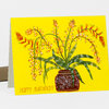 A folded greeting card with a bright yellow cover showing a potted cactus-like plant with long green leaves and orange-and-white flowers, and the text "HAPPY BIRTHDAY!" at the bottom.