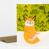A greeting card with the text "HAPPY BIRTHDAY!" and an illustration of an orange fox in a green forest scene, with a brown envelope partially visible behind it.