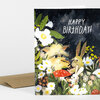 A folded greeting card with a floral garden scene featuring whimsical creatures, including rabbits and a fuzzy animal, and the text "HAPPY BIRTHDAY!" on the front.