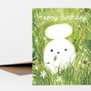 A folded greeting card with the text "Happy Birthday!" above a white bunny illustration surrounded by green grass and small flowers.