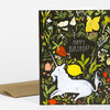 A folded greeting card with a black cover illustrated with flowers, greenery, a white unicorn, a small yellow fairy figure, and the text "HAPPY BIRTHDAY".