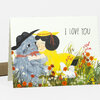 A folded greeting card featuring an illustration of a girl hugging a beast in a flowered field with the text "I LOVE YOU" on the front.