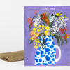 A greeting card with a purple cover showing a blue-and-white spotted vase of flowers and the text “I LOVE YOU!” at the top.