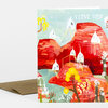 A folded greeting card with an illustrated landscape of red rock formations, small white houses on stilts, flowers, and the text "I LOVE YOU!" on the front, with a kraft-colored envelope behind it.