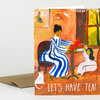 A folded greeting card with an illustrated tea scene showing two seated figures, a red teapot, a small white cat, and the text "LETS HAVE TEA!" on the front.