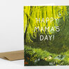 A folded greeting card with an illustrated green garden scene and the white text "HAPPY MAMA'S DAY!" on the front.