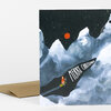 A folded greeting card with an illustrated snowy mountain scene, a small skier in orange, and the text "MERRY CHRISTMAS" on the front.