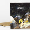 A folded greeting card with the text "NEW HOME, NEW CHAPTER" on the front and an illustrated night landscape with mountains, trees, and a yellow house.