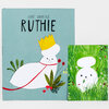 A hardcover book titled "RUTHIE" by Esmé Shapiro with a blue cover showing a white rabbit wearing a yellow crown and red necklace, plus a smaller matching illustrated book or card with a rabbit in green grass.