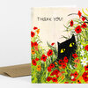 A greeting card with the text "THANK YOU!" and an illustration of a black cat with yellow eyes peeking through red and orange flowers and green grass.