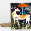 A folded greeting card shows an illustrated white llama or alpaca wearing colorful decorations and carrying a small carousel with two blue figures, with the text "to the LOVELY COUPLE!" on the front.