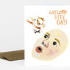 A folded greeting card with the text "WELCOME, LITTLE ONE!" and an illustration of a baby face with small floating figures above it.