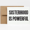 A folded greeting card with a kraft envelope, featuring the bold black text "SISTERHOOD IS POWERFUL" on the front.