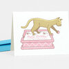A folded greeting card showing a yellow cat walking across a pink birthday cake with the words “Happy Birthday!” on the cake.