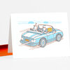 A folded greeting card with a blue convertible car illustration showing two dogs inside, one holding a birthday cake, and the license plate text "HPYBDY".