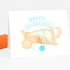 A folded greeting card with an orange cat illustration wrapped in blue yarn and the words "HAPPY BIRTHDAY" above it.
