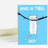 A blue greeting card showing a white cat hanging from a black branch with the text "HANG IN THERE, BABY" in white letters.