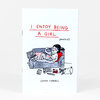 A small folded zine with a white cover that reads "I ENJOY BEING A GIRL (MOSTLY)" and "GEMMA CORRELL," featuring a cartoon person lounging on a couch with a laptop and snack bag.