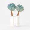 A small desk calendar shaped like two green succulent plants growing from a white planter, with a March month grid printed on the left plant.