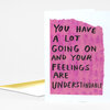 A folded white greeting card with a pink painted rectangle on the front and hand-lettered black text reading "YOU HAVE A LOT GOING ON AND YOUR FEELINGS ARE UNDERSTANDABLE".