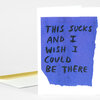 A folded greeting card with a blue torn-paper-style rectangle on the front and handwritten black text that reads, "THIS SUCKS AND I WISH I COULD BE THERE."