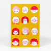 A postcard with a yellow front printed with twelve simple red-and-white cartoon faces with different hairstyles and one pair of glasses.