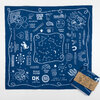 A blue Western-themed bandana-style handkerchief with white illustrated icons and phrases, including cowboys, horseshoes, cacti, a snake, and a star map, plus a small product tag attached.