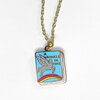 A gold-tone chain necklace with a small book-shaped enamel charm showing the text "A WRINKLE IN TIME" and an illustration of a winged horse over a rainbow.