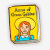 A book-shaped pin with a yellow cover reading "Anne of Green Gables" and an illustration of a red-haired girl in a hat.