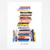 A white tea towel printed with a stack of illustrated baking-themed book spines arranged like a bookshelf, with the title "IDEAL BOOKSHELF" near the bottom.