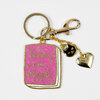A gold-tone keychain with a pink glitter book-shaped charm that reads "Books are Magic," plus a small black cat charm and a gold heart charm.