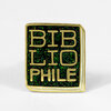 A square enamel pin shaped like a book with gold lettering that reads "BIBLIOPHILE" on a black and green glitter background, outlined in gold.