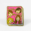 A pink enamel pin shaped like a book cover with gold-outlined text reading "Little Women" and four illustrated female faces.
