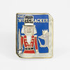 A rectangular enamel pin with gold-tone outlines shows a nutcracker figure, a mouse holding a sword, and the text “THE NUTCRACKER.”
