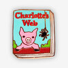 A small enamel pin shaped like a book cover with the text "Charlotte's Web," featuring a pink pig and a hanging spider illustration.