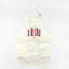 A cream-colored apron with neck and waist straps, two front pockets, and a small graphic of colorful cookbook spines with text near the chest.