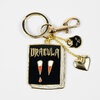 A gold-tone keychain with a large book-shaped charm that says "DRACULA" and has a stylized vampire face, plus a small black skull charm and a gold heart charm.