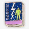 A rectangular enamel-style pin shaped like a book cover with the word "FRANKENSTEIN" printed vertically, a white lightning bolt, and a green Frankenstein figure on a blue and pink design.