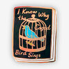 A rectangular enamel pin with rounded corners shows a blue bird inside a gold cage and the text "I Know Why the Caged Bird Sings."
