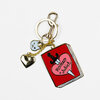 A gold-tone keychain with a red book-shaped charm reading "Romeo + Juliet," a pink heart with a sword graphic, a small silver heart charm, and a small blue face charm.