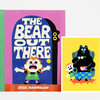 A colorful hardcover book titled "THE BEAR OUT THERE" by Jess Hannigan, with a pink and blue cover showing a surprised child and a black bear shape, plus a small matching illustrated card or insert beside it.