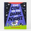 A hardcover book titled "THE COW IN THE DARK AT NIGHT" with a purple-and-black cover showing stars, grass, and a cow illustration, and the author name "JESS HANNIGAN" at the bottom.