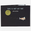 A black hardcover book titled "THIS IS NOT MY HAT" by Jon Klassen with a gold medal seal and a small illustrated fish wearing a hat on the cover.