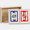 A wooden box set holding two playing card decks, one with a blue magician design and one with a red fool design.