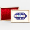 A wooden box set with two shallow rectangular trays, one lined with red velvet and one with a cream lid decorated with a blue royal-style emblem and five printed dice-like tiles.