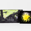 A picture book titled "In the DARK" with cover art showing two children in a dark forest under a yellow-green sky and the text "text by Kate Hoefler art by Corinna Luyken," alongside a square insert or companion image of silhouetted figures around a bright yellow moon.