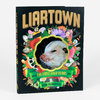 A hardcover book with a black cover featuring the large title "LIARTOWN," a central opossum face inside a scalloped frame, and the text "THE FIRST FOUR YEARS" and "SEAN TEJARATCHI" on green banners.
