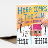 A folded greeting card with a winter scene illustration and the text "HERE COMES THE SUN" and "HAPPY SOLSTICE" on the front.